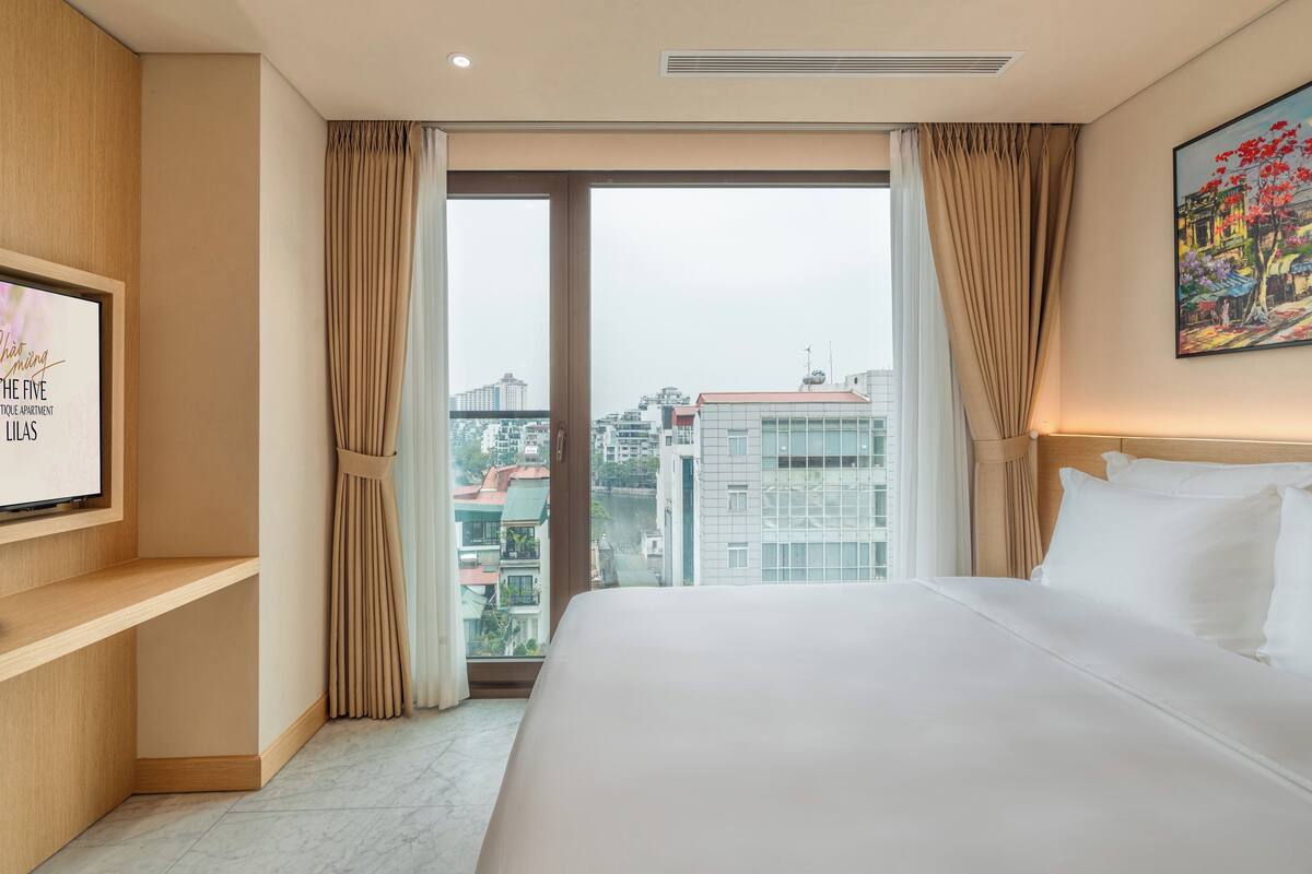 Habitación de hotel con una cama grande, un televisor en la pared, vistas de la ciudad y un cuadro.