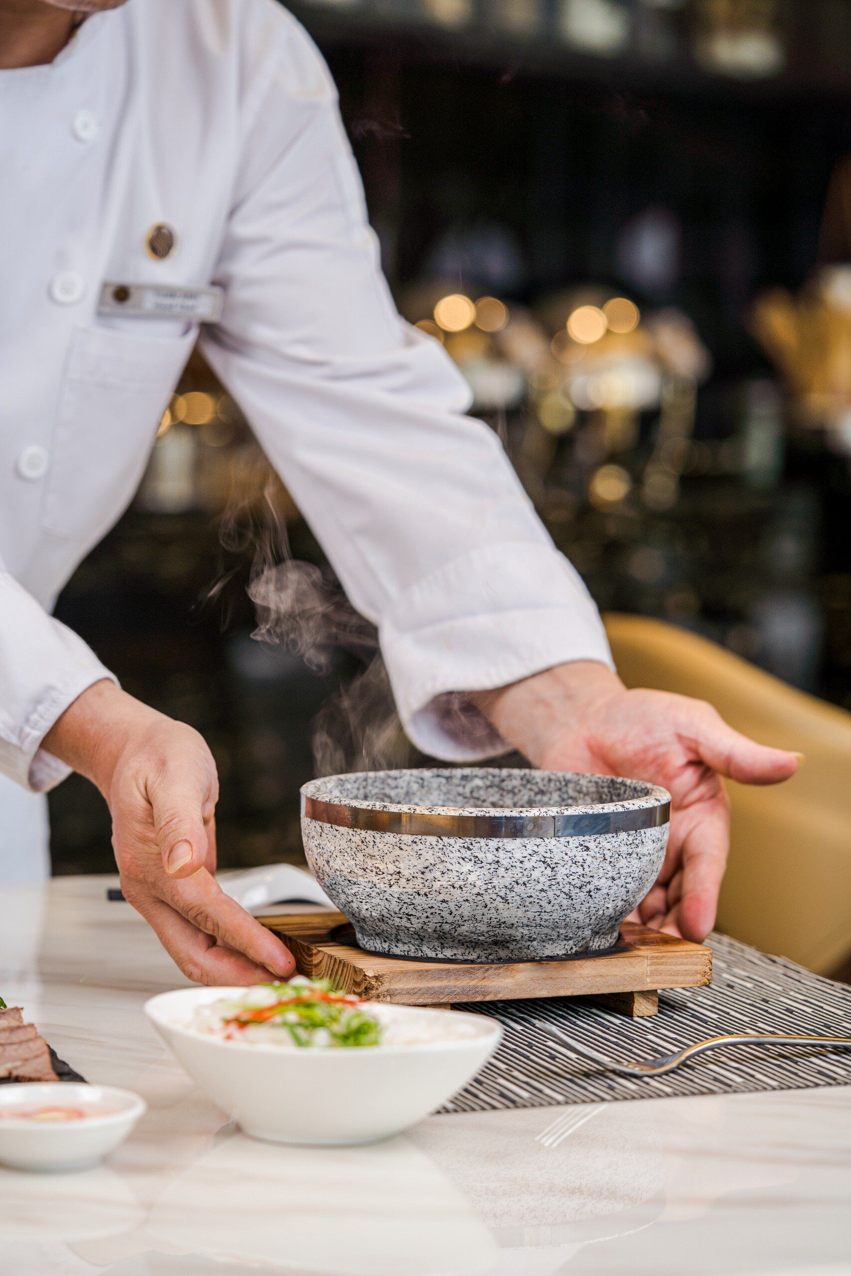 Un chef sosteniendo un bol con vapor saliendo, sobre una tabla de madera.
