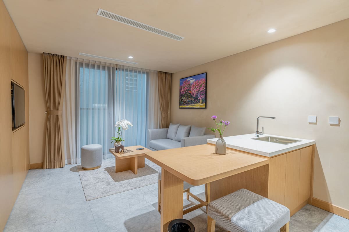 Un espacio habitable pequeño con kitchenette, un sofá, una mesita y una ventana con cortinas.