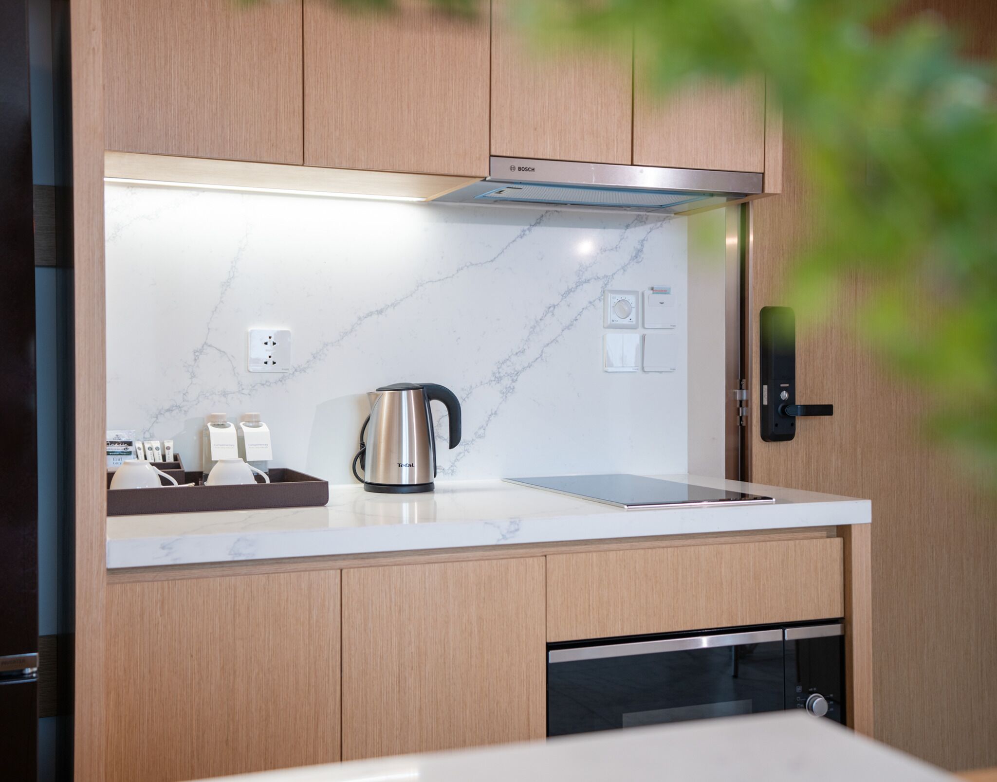 A modern kitchen with a stainless steel kettle, a built-in oven, and wooden cabinets.