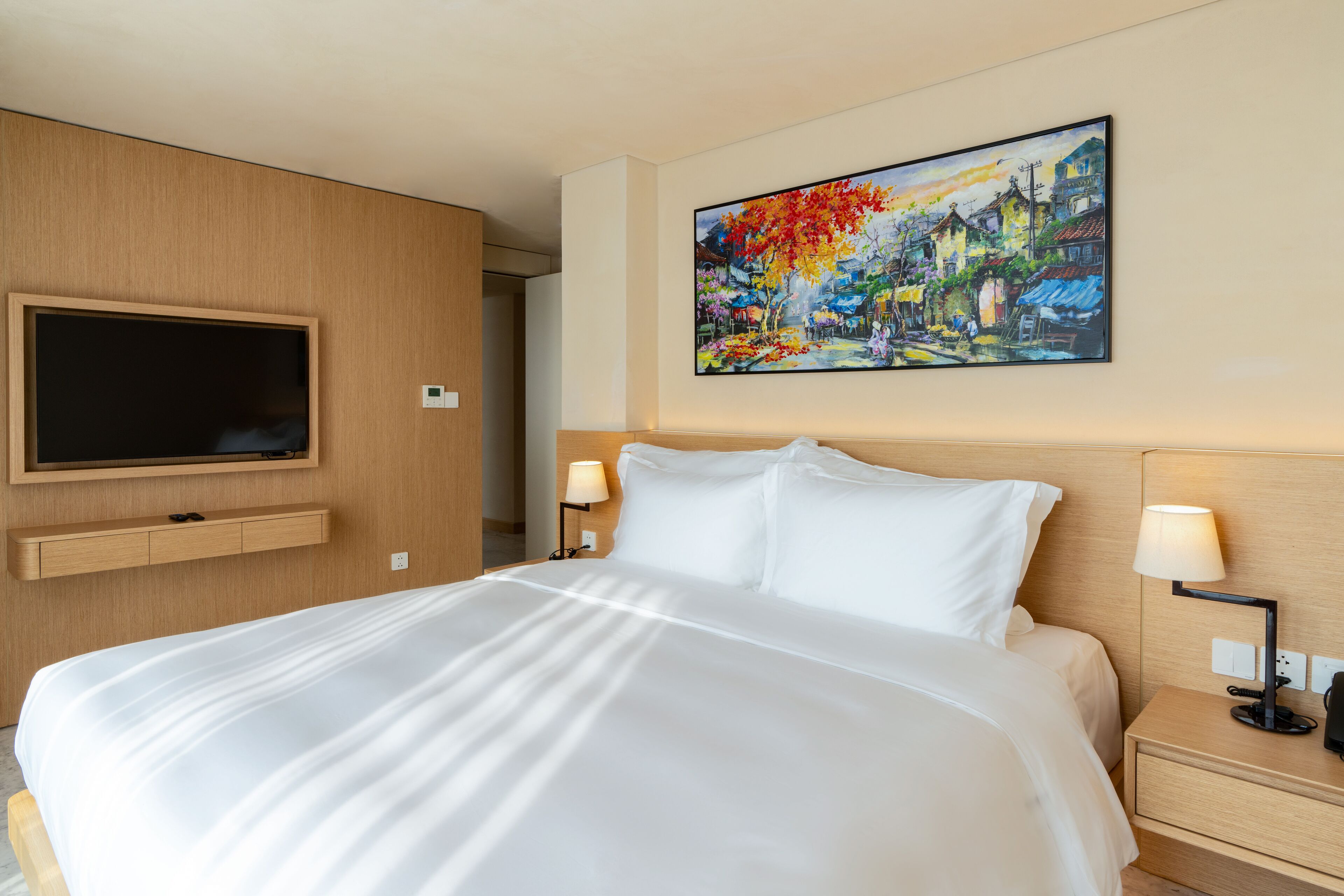 Une chambre d’hôtel avec un grand lit, un téléviseur fixé au mur, des lampes de chevet et un tableau accroché au mur.