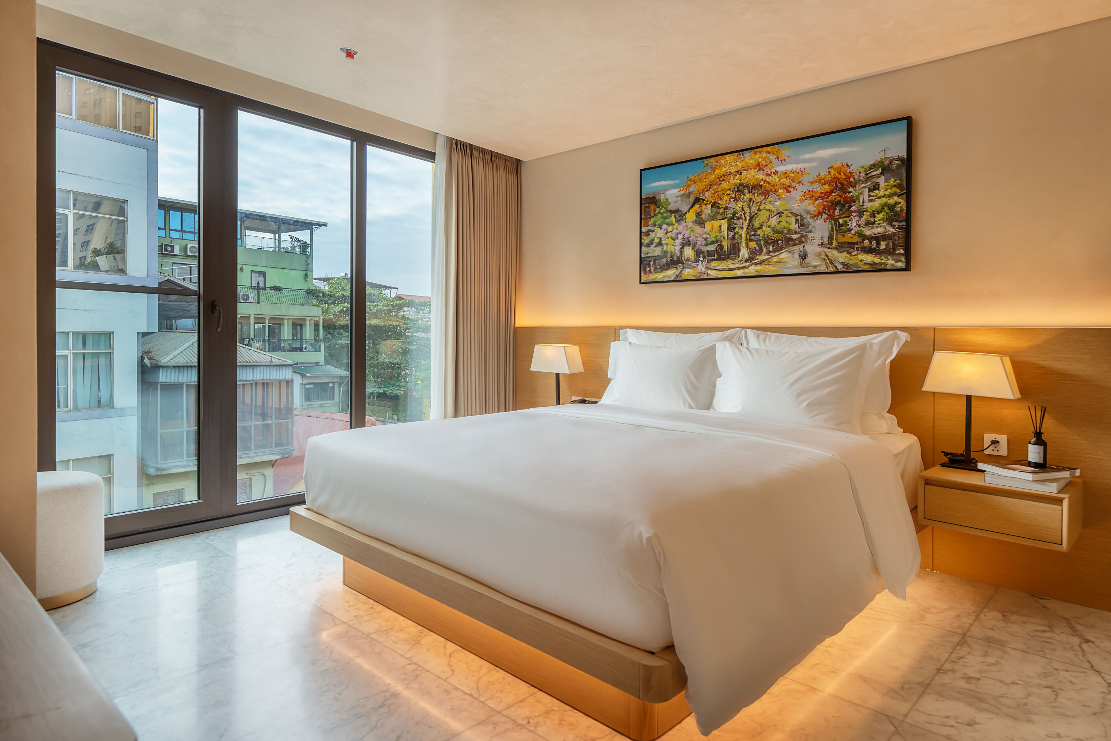 A modern hotel room with a large bed, a nightstand with a lamp, and a painting on the wall.