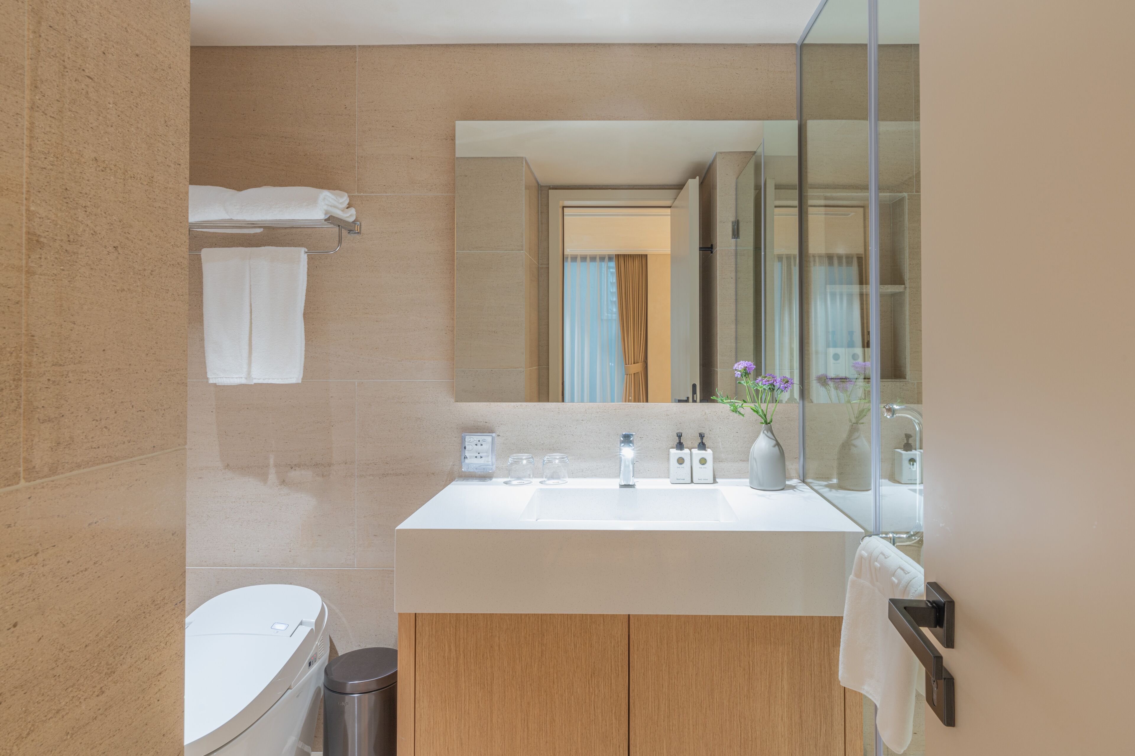 A modern bathroom with a large mirror, a white sink, and a toilet.