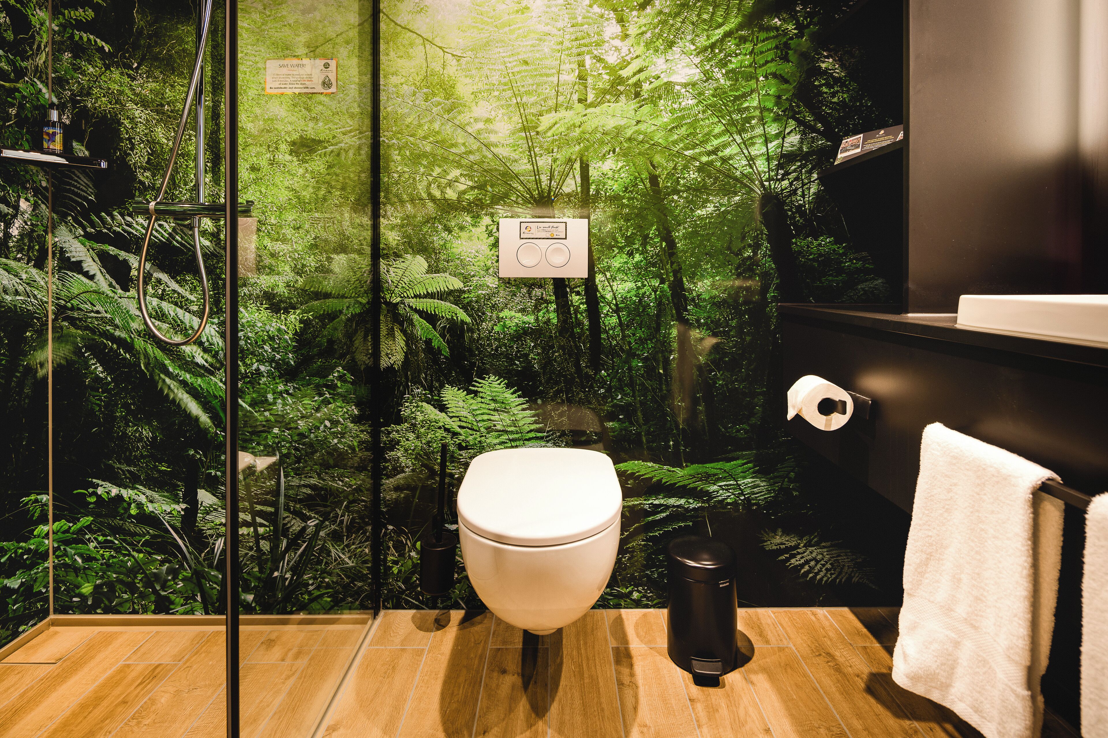 A bathroom with a toilet, a hand dryer, a trash bin, and a towel rack.