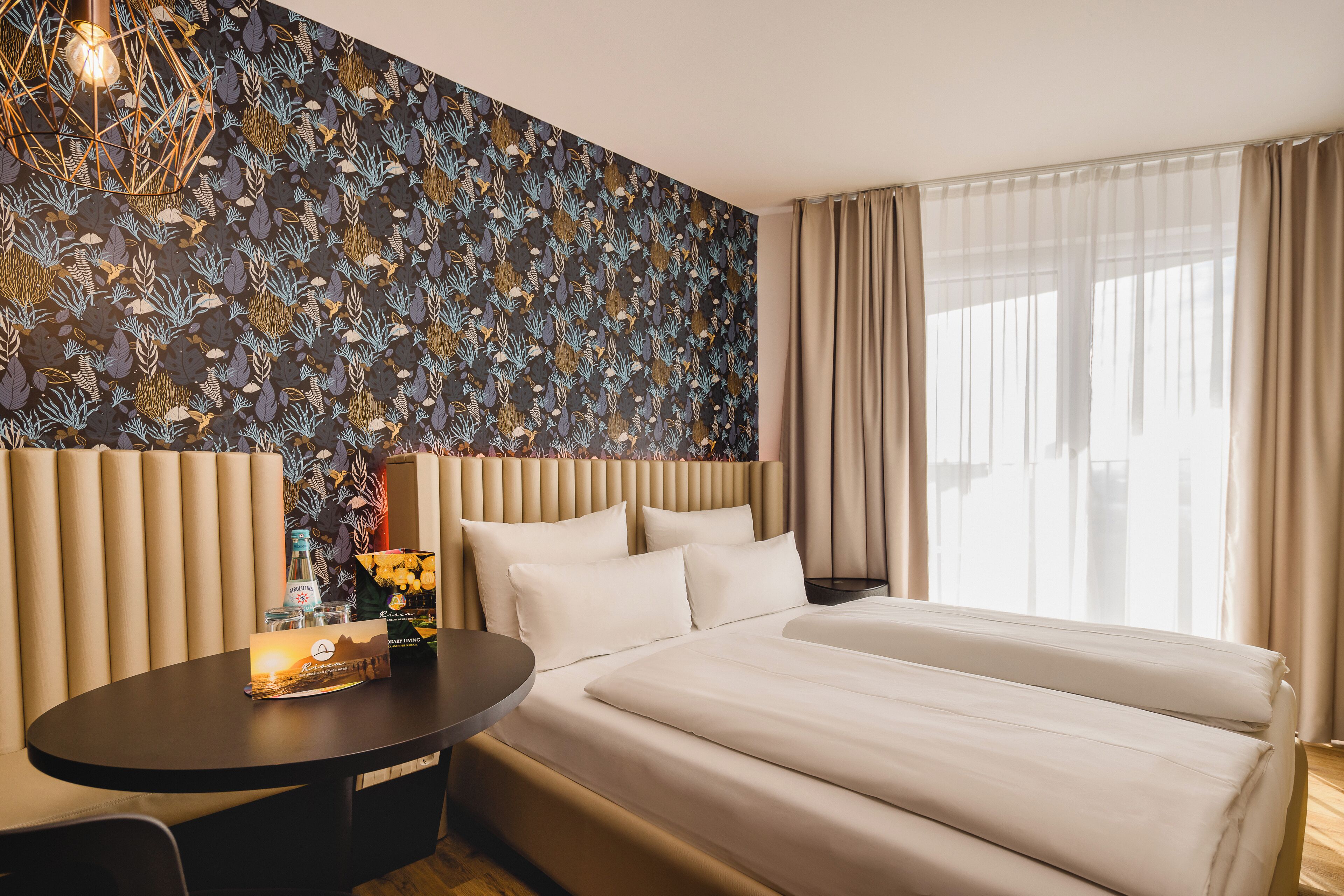 A hotel room with a large bed, a round table with a lamp, and a patterned wall.