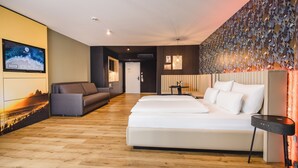 Moderni hotellihuone, jossa on puulattia, sohva, sänky, televisio ja koristeellinen seinä.