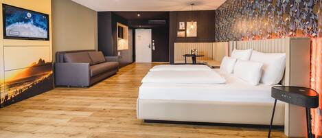 Ett modernt hotellrum med trägolv, en soffa, en säng, en tv och en dekorativ vägg.
