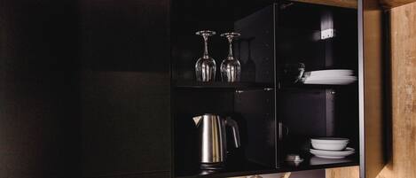 A kitchen with a black cabinet, a stainless steel kettle, wine glasses, and white plates.