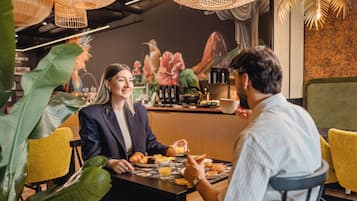 Un comedor con una mesa dispuesta para dos personas, que incluye diversas opciones de desayuno y una cafetera.