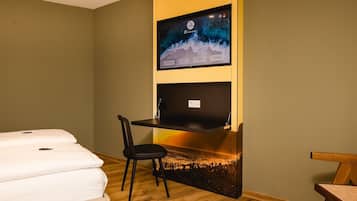 A hotel room with a bed, a desk, a chair, and a TV mounted on the wall.