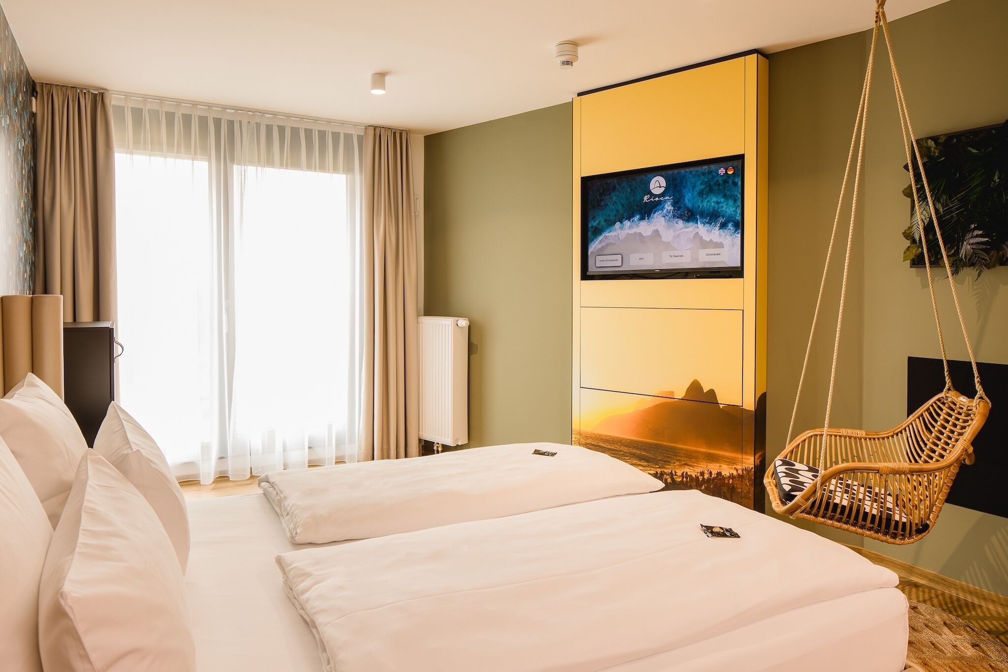 Habitación de hotel con dos camas, un televisor en la pared, una silla colgante y vistas a un atardecer.