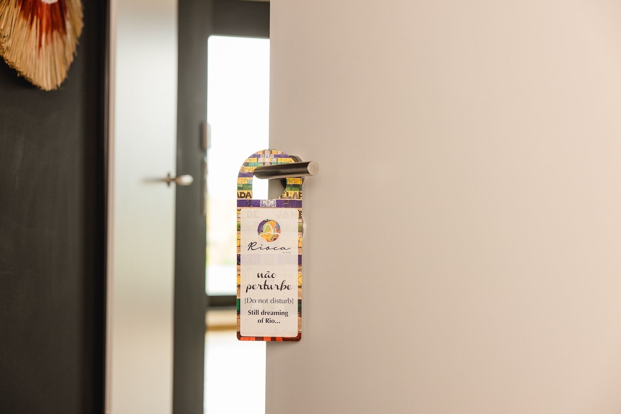 A door with a hanging sign that reads "Ríoca" and "não perturbe" with a translation "Do not disturb" and "Still dreaming of Rio...".