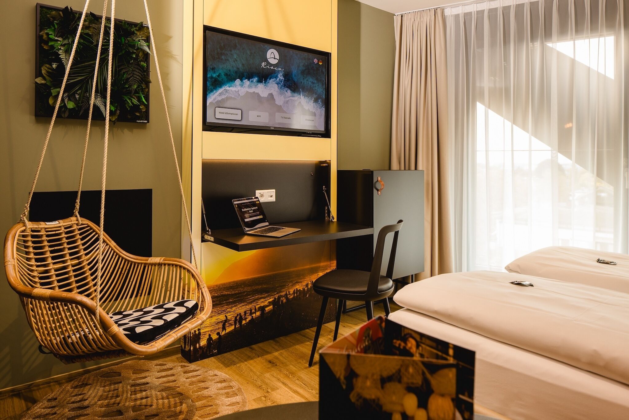 Una habitación de hotel moderna con una cama, una silla colgante, un escritorio con una computadora portátil, un televisor en la pared y una ventana con cortinas.