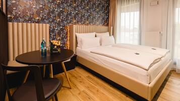 A hotel room with a bed, a small table with chairs, a decorative wall, and a window with curtains.
