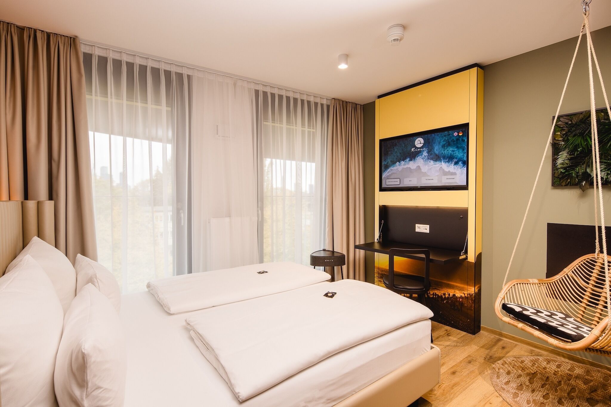 A modern hotel room with a large bed, a TV, a desk, and a hanging chair.