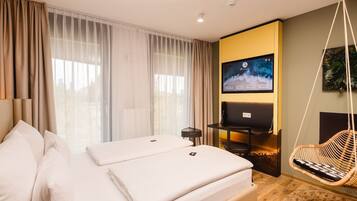 A modern hotel room with a large bed, a TV, a desk, and a hanging chair.