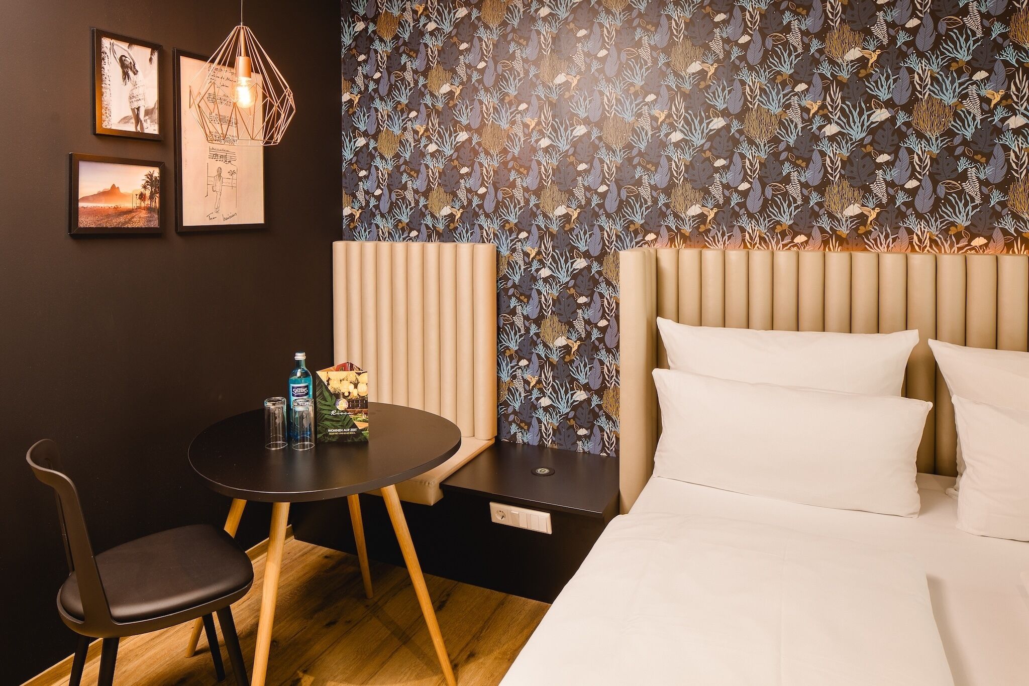 Una camera d'albergo con un letto, una scrivania con una sedia, e una parete decorata con quadri e carta da parati a motivi.