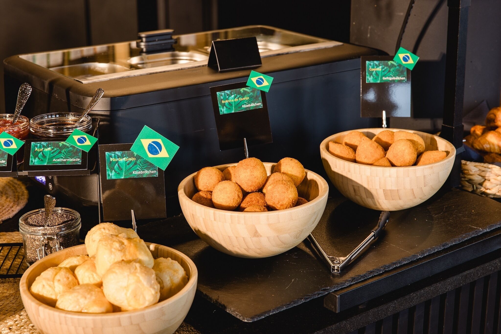 Buffet amb diferents plats brasilers, incloent pa de queijo i bolinhos de queijo, servits en bols de fusta.