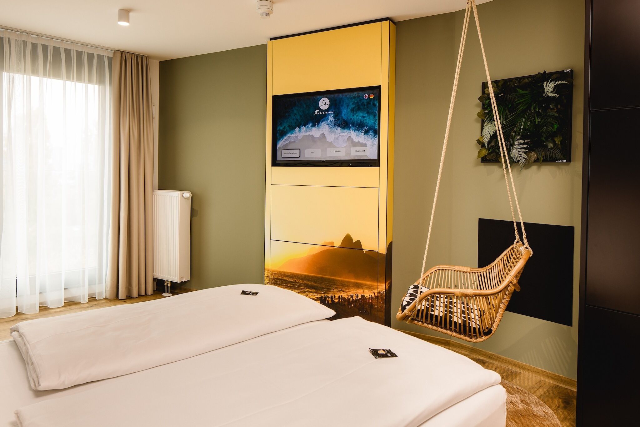 A hotel room with a bed, a television mounted on the wall, a hanging chair, and a large window with curtains.