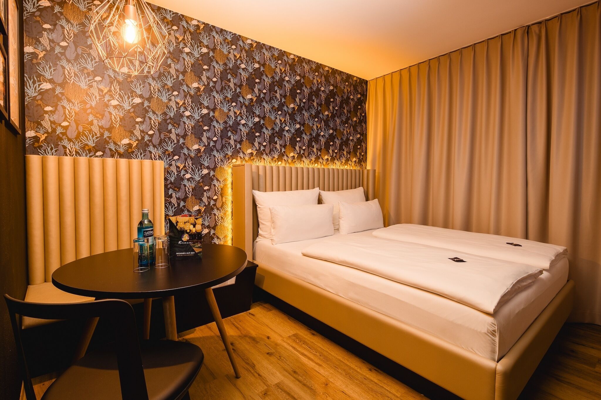 Una camera d'albergo con un letto, un tavolo rotondo e un muro decorato.