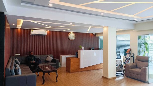 Un área de recepción moderna con un mostrador de madera, un reloj y una zona de estar con un sofá y una mesa de centro.