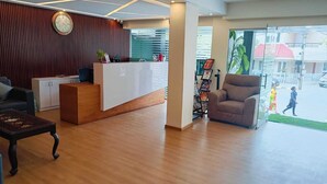 Una zona de recepción con un mostrador de madera, un reloj y un área de estar con un sofá y sillones.