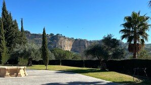 A paved courtyard with a stone bench, a palm tree, and cypress trees. - Hotel La Hoya del Tajo (Ronda)