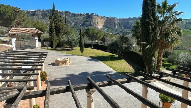 A terrace with a view of a mountainous landscape, featuring a pergola, potted plants, and a paved area. - Hotel La Hoya del Tajo (Ronda)