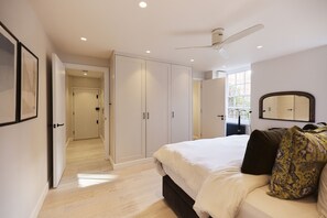 A bedroom with a bed, a ceiling fan, and a large wardrobe.