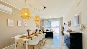 Een moderne eethoek met een lange tafel, witte stoelen en gevlochten hanglampen.