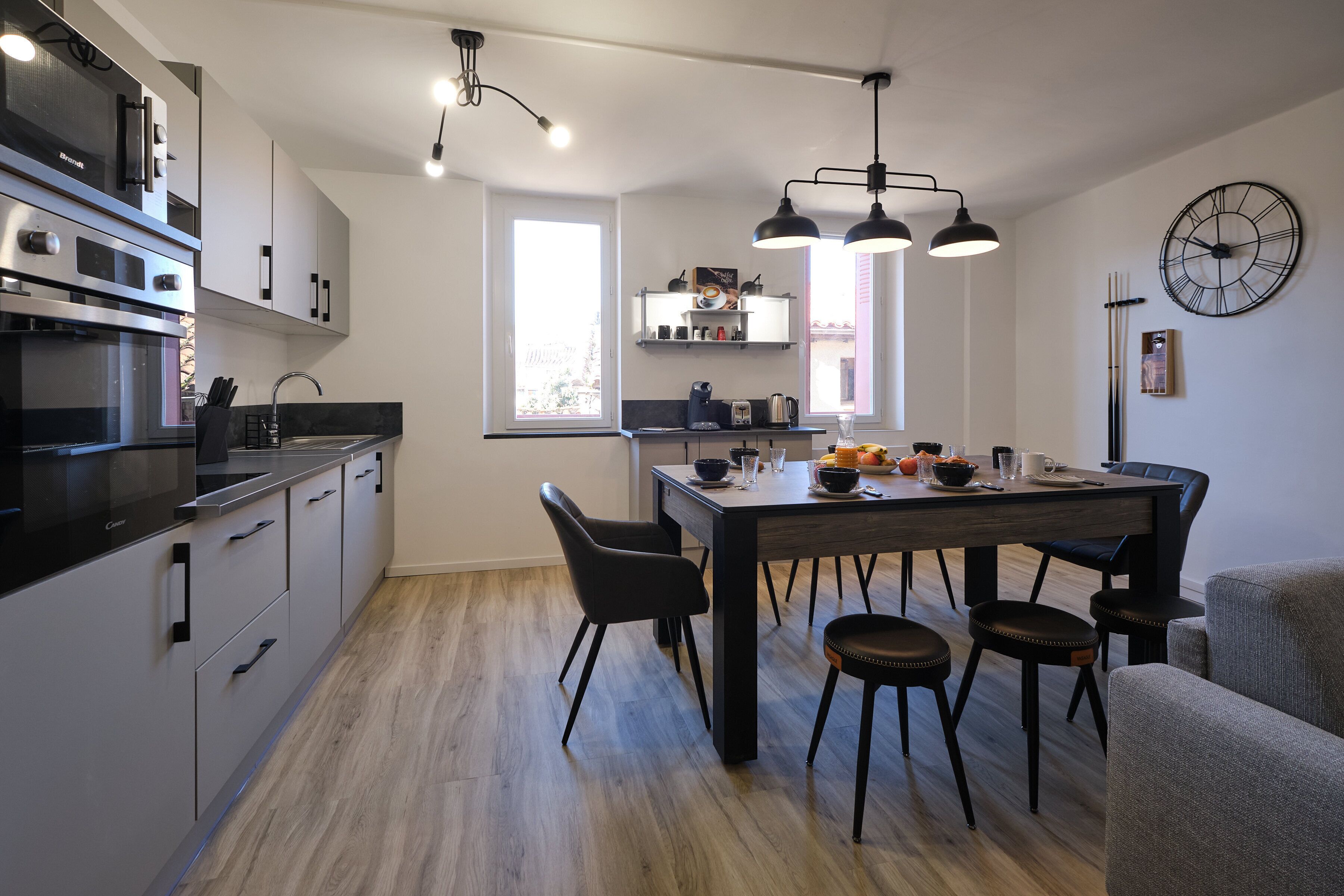 A modern kitchen with a dining area, featuring a large window, built-in appliances, and a clock on the wall.