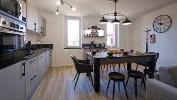 A modern kitchen with a dining area, featuring a large window, built-in appliances, and a clock on the wall.