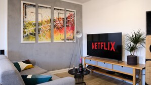 Una sala de estar moderna con un televisor de pantalla plana grande, un sofá, una mesa de centro con copas de vino y una planta en maceta.