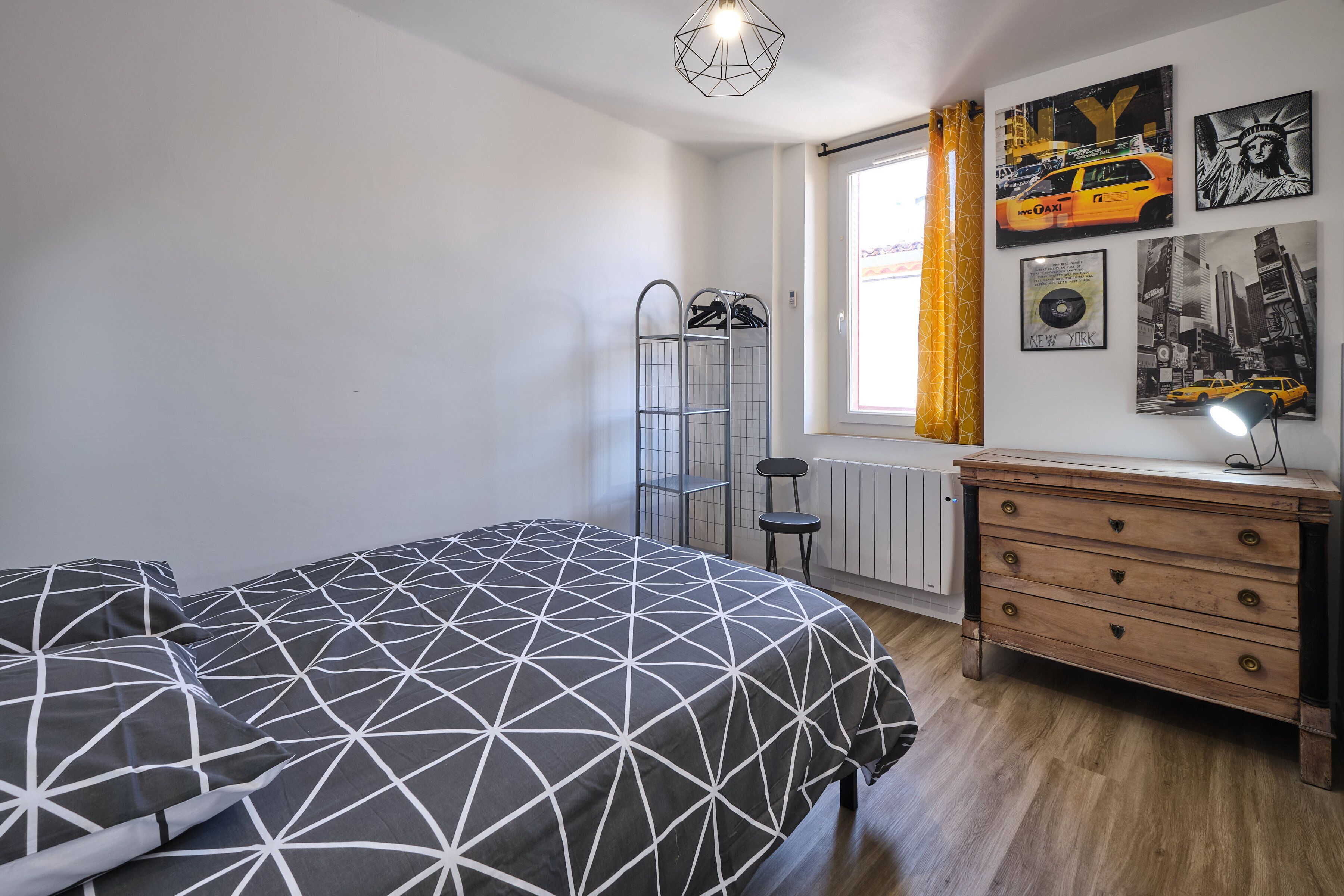 Un dormitorio con cama, cómoda, radiador y ventana con cortinas.