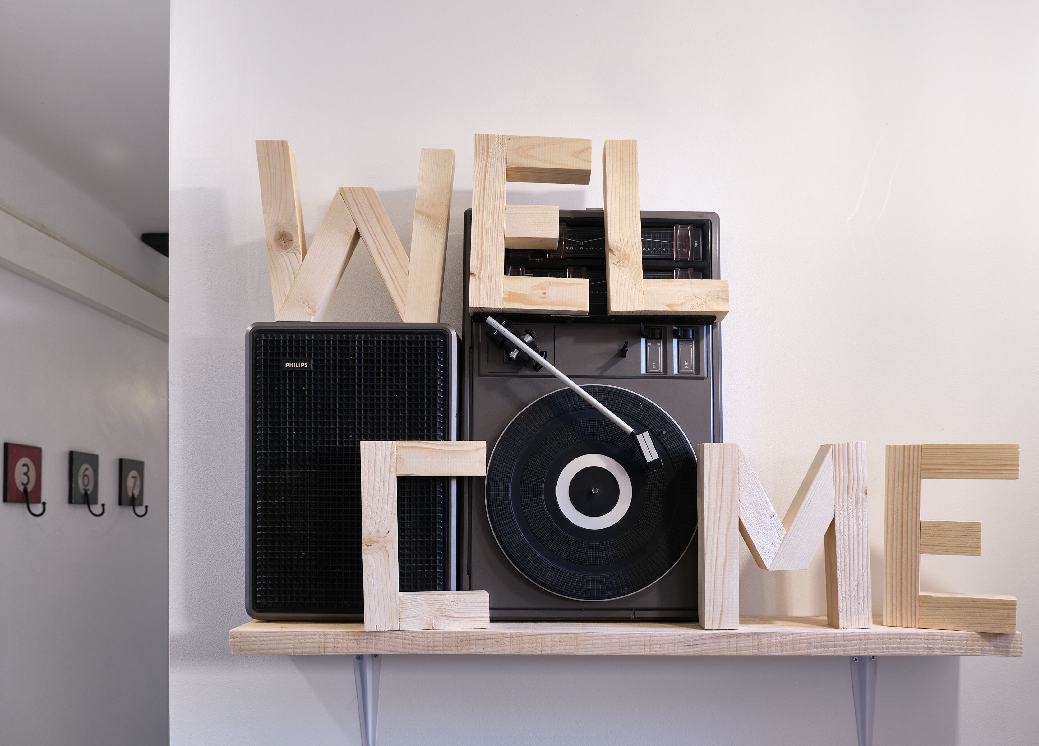 Una estantería montada en la pared con un tocadiscos, un altavoz y letras de madera que dicen "WELCOME".