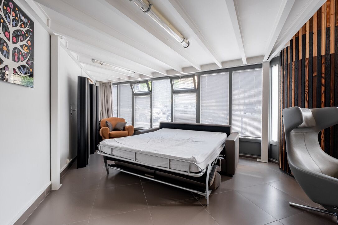 A modern bedroom with a foldable bed, a gray chair, and large windows.