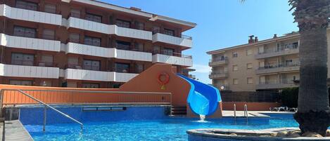 A swimming pool with a water slide, surrounded by multi-story buildings with balconies.