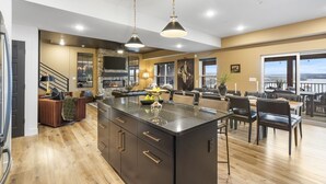 Une cuisine spacieuse dotée d’un grand îlot central, de luminaires suspendus modernes et offrant une vue sur l’extérieur.