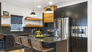 Une cuisine moderne avec des meubles de couleur sombre, des appareils en acier inoxydable et un îlot central doté de tabourets de bar.