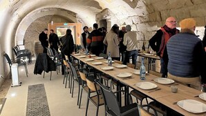A long table with chairs, a stone wall, and people standing.