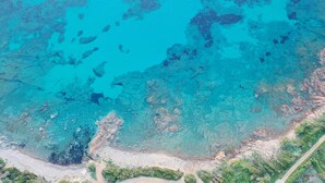 Vue aérienne d’une zone côtière caractérisée par des eaux turquoise limpides, des côtes rocheuses et une végétation luxuriante.