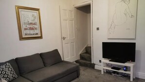 Ein Wohnzimmer mit grauem Sofa, einem Fernseher auf einem Schrank und einer Tür zu einem weiteren Raum.