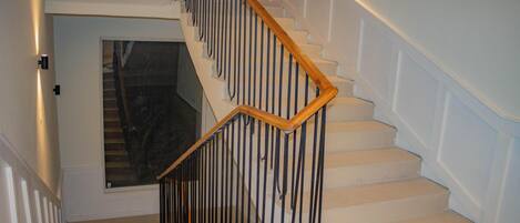 A staircase with a wooden handrail and metal balusters, leading to a landing with a glass door.