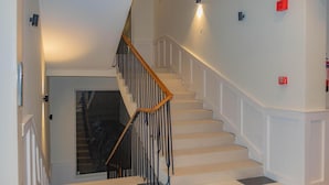 Un escalier avec des rampes blanches et une main courante en bois, menant à un palier doté d’une porte en verre.