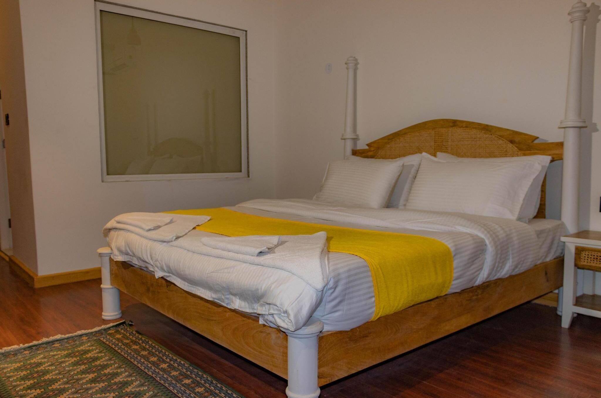 A neatly made bed with a wooden frame, white bedding, and a yellow throw blanket.