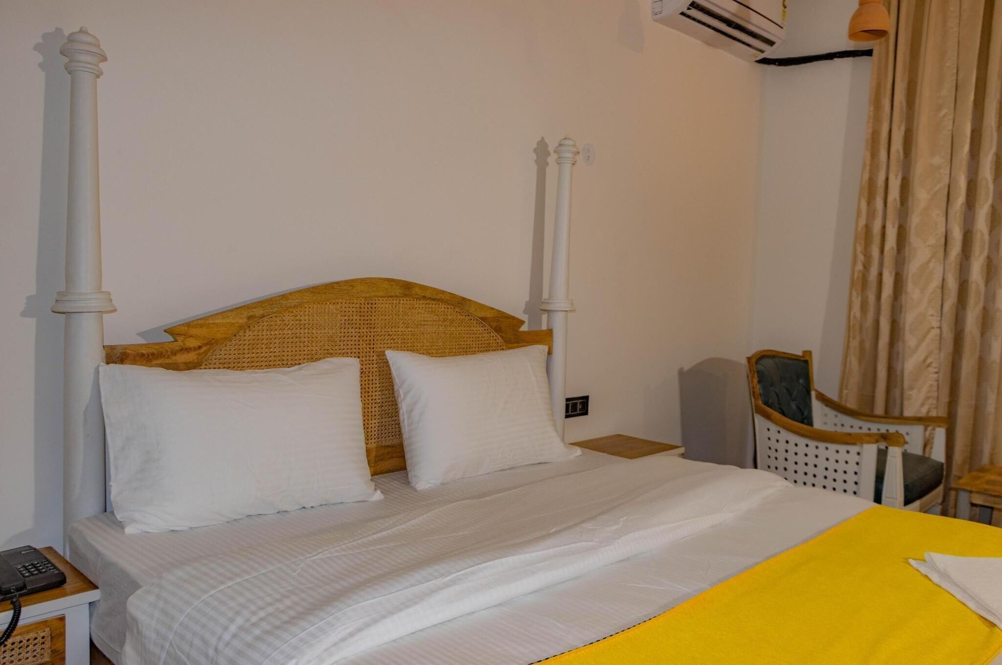 Una cama bien hecha con sábanas blancas, cabecera de madera y colcha amarilla.