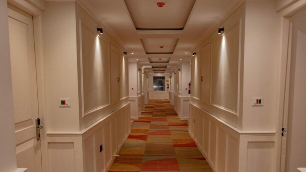 Un couloir d’hôtel avec un tapis à motifs, des murs blancs et des portes de chaque côté.