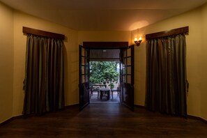 A hallway with wooden flooring leading to an open door, flanked by curtains and a table with chairs.