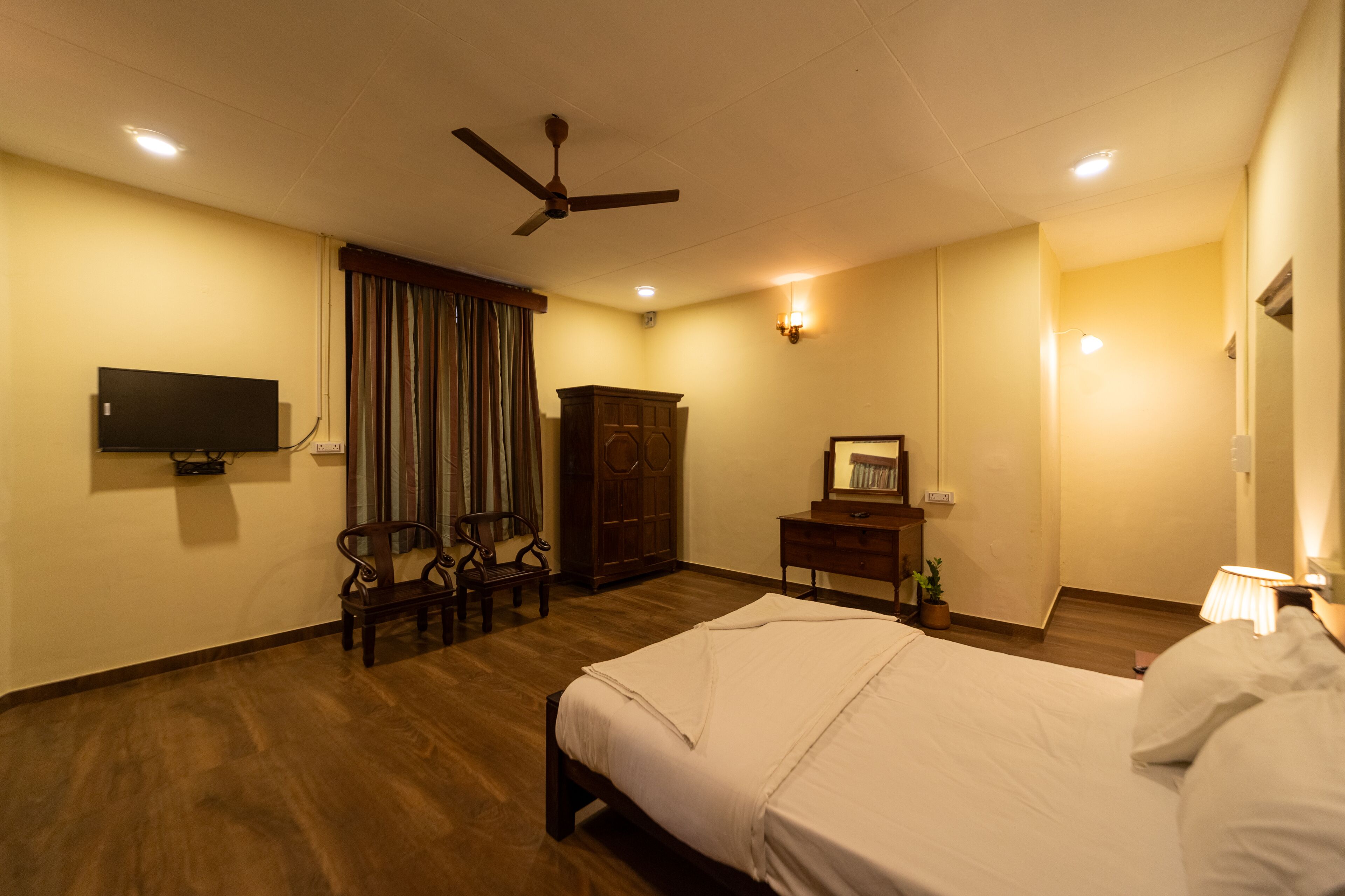A hotel room with a bed, a desk, a chair, a wardrobe, a television, and a ceiling fan.