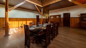 Une salle à manger spacieuse avec un plafond haut et des poutres en bois, où trône une grande table en bois, dressée pour le repas.